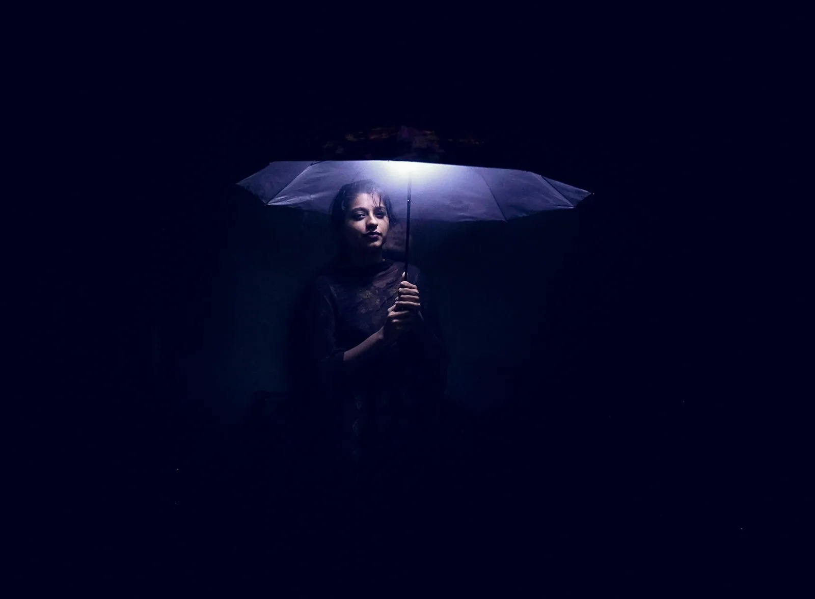 A woman under an umbrella in blue night light