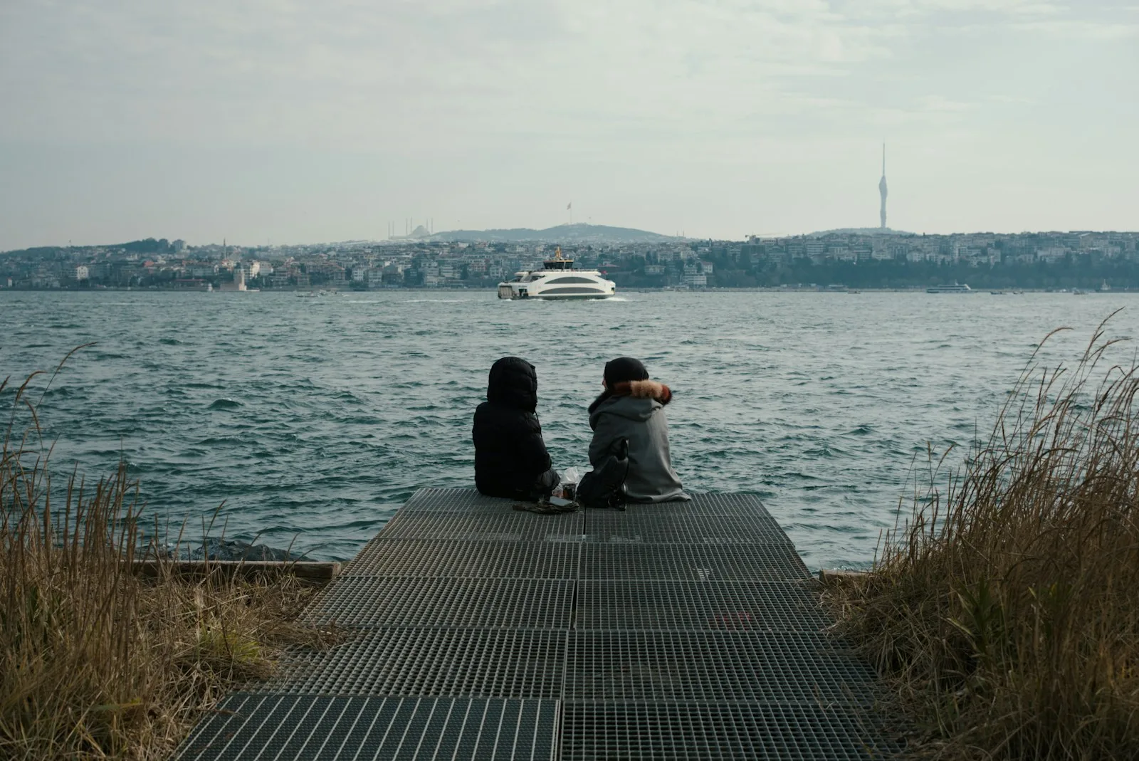Two people on a pier looking out at the water